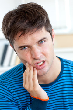 Cute caucasian man having a toothache in the living-room