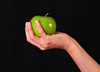 A female hand holding a green apple, black background