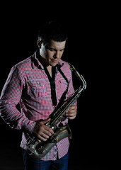 Naklejka premium Young handsome man playing music on saxophone. black background