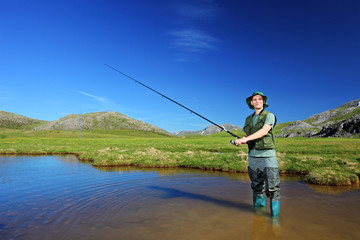 Happy fisherman fishing at lake with mountains in the background
