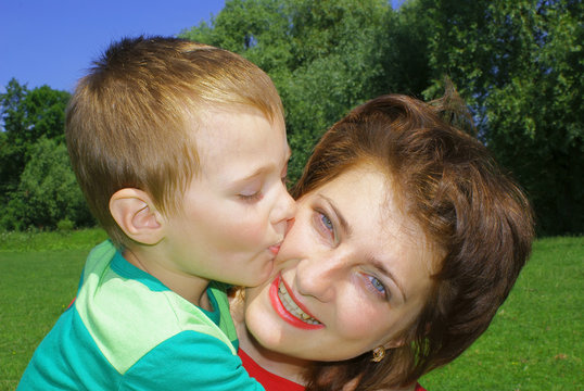 A little boy kisses his mom on the cheek, background nature