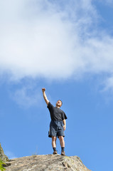A young man stands on a cliff top and raised his hands