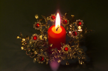 Brennende rote Kerze in einem goldenen Pflanzengeflecht