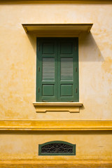Fototapeta na wymiar green window shutters on yellow wall with great shadows
