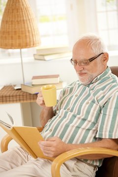 Elderly man reading book and having tea.