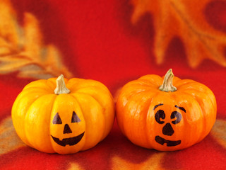 Mini Pumpkins with Funny Faces on a Red Autumn Cloth Background