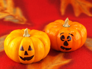 Mini Pumpkins with Funny Faces on a Red Autumn Cloth Background