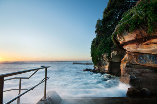 rocky coastal view with rushing wave and handrail beside