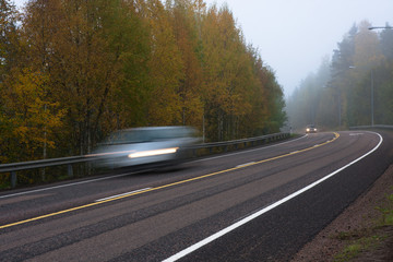 Dangerous mist on country road in forest with fast moving cars