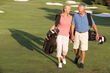 Afwasbaar Fotobehang Golf Senior koppel wandelen langs de golfbaan met tassen