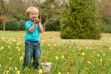 A toddler smiles while proudly holding an Easter egg