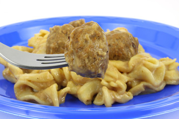 Meatball on fork with pasta on blue plate