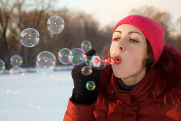 Girl blow bubbles in winter park. She is wearing jacket and hat.