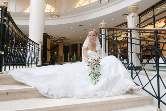Bride in wedding dress sits on staircase with bunch of flowers