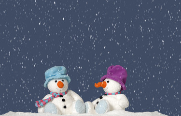 snowing on 2 snowmen sitting in the snow