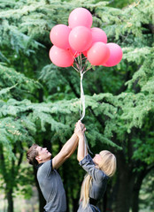young loving couple with red balloons on natural background