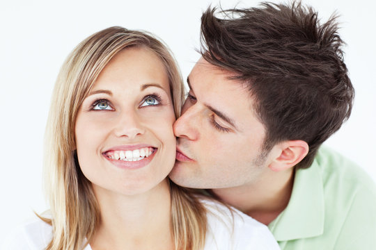 Careful man kissing his smiling girlfriend against a white backg