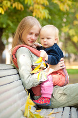 Young adorable woman and cute baby with leafs sitting on bench i