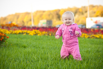 Cute cheerful baby walking on green grass among variety of flowe