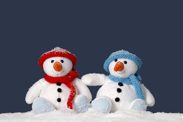 two cute snowmen sitting in the snow
