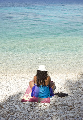 Asian woman sitting on a pebbly beach.