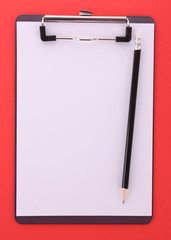 Clipboard and pencil on red background