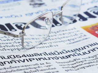 Close-up of Thai language newspaper and a pair of glasses