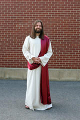 Man in Jesus robe and sash next to brick wall