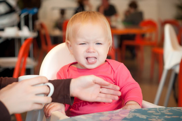 Adorable toddler girl sitting on chair in cafe with mother
