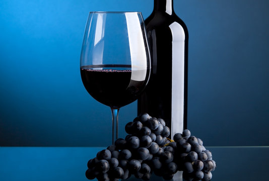 A glass of red wine with bottles and grapes on a blue background