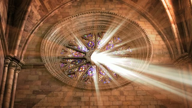 Sunlight beams through a circular stained glass window in a cathedral, casting rays of light. Perfect for spiritual, architectural, and historical projects.