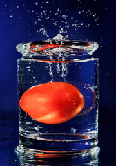 Tomate rouge tombant dans le verre avec de l& 39 eau sur un bleu profond