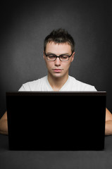 serious young man using laptop on black background