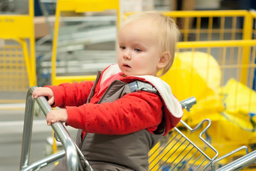 Cute toddler girl sit on shopping cart in mall
