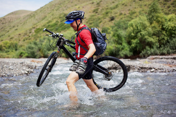 Biker goes over the mountain river ford