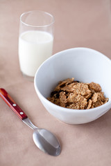 bowl of cornflakes and glass of milk on beige tablecloth