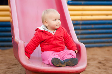 Fototapeta na wymiar Cute toddler girl sit on side after slide down from top of slide