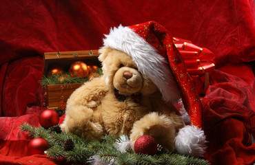 A teddy bear in a Christmas hat on a red silk background