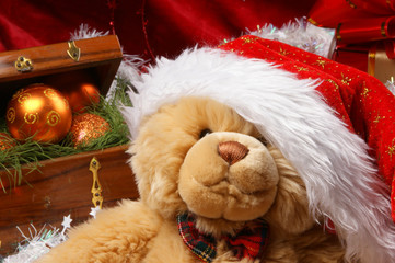 A teddy bear in a Christmas hat on a red silk background