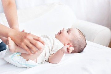 Cute baby smiling while his mother is changing his nappy in the