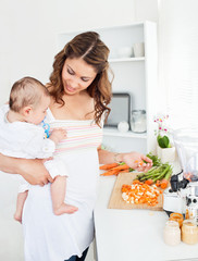 Obraz na płótnie Canvas Młoda matka trzyma jej dziecko podczas przygotowywania marchewkę na obiad