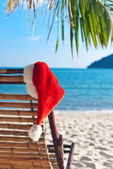 Red Santa's hat hanging on beach chair under palm tree