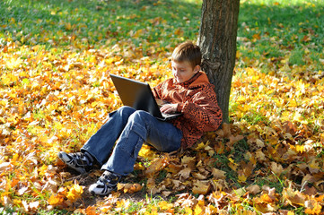 Child make fun with laptop under tree in autumn forest