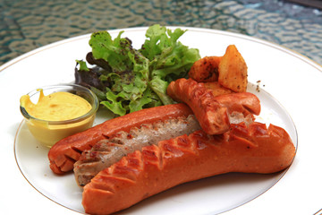 Appetizing grilled sausages with green salad and mustard sauce