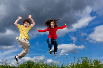 Girl and boy jumping, running against blue sky