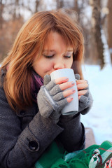 pretty girl drinking hot tea in winter park