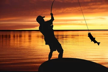 Abwaschbare Fototapete Angeln Fischer mit einem fangenden Fisch auf Sonnenaufgang Hintergrund