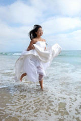 Fototapeta na wymiar Bride Running Through the Ocean in Wedding Dress