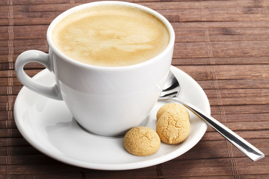 kaffee in einer weissen tasse mit einem l&ouml;ffel und amarettini