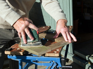 Sanding, electric sander in right hand on wood